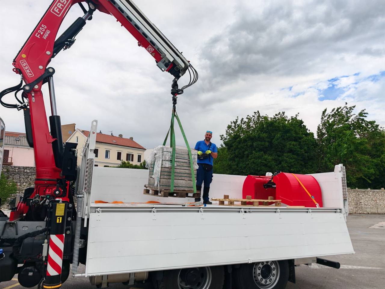 Radnik uz kamion s kranom podiže materijal